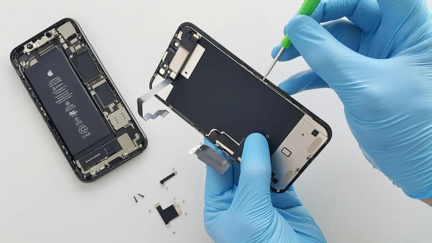 Técnico de luvas azuis abrindo um celular para o conserto